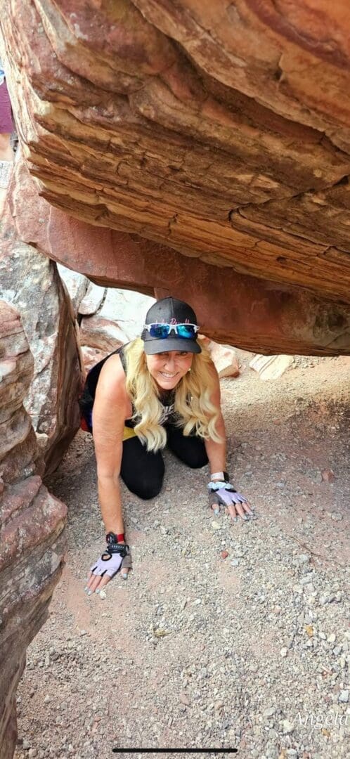 A woman kneeling down under a large rock.