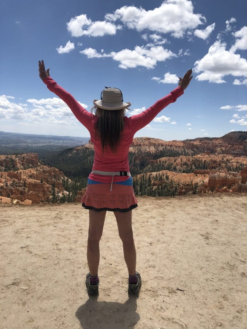 A woman standing on top of a hill with her arms in the air.