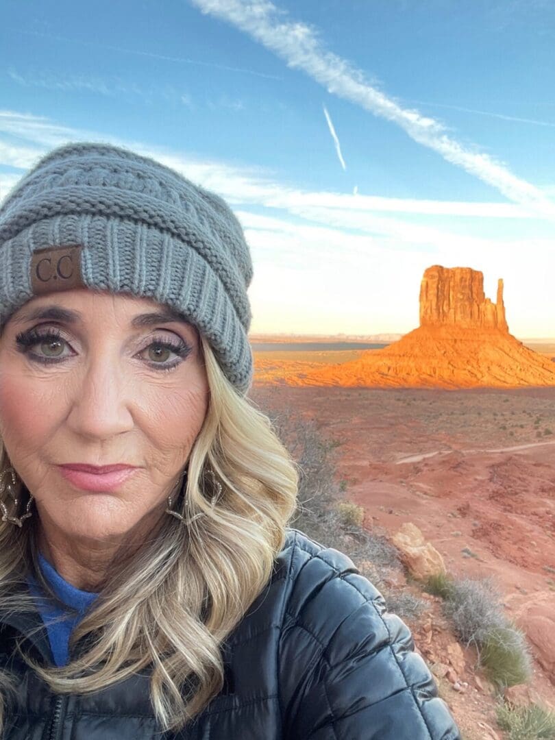 A woman in a hat and jacket standing on the side of a road.