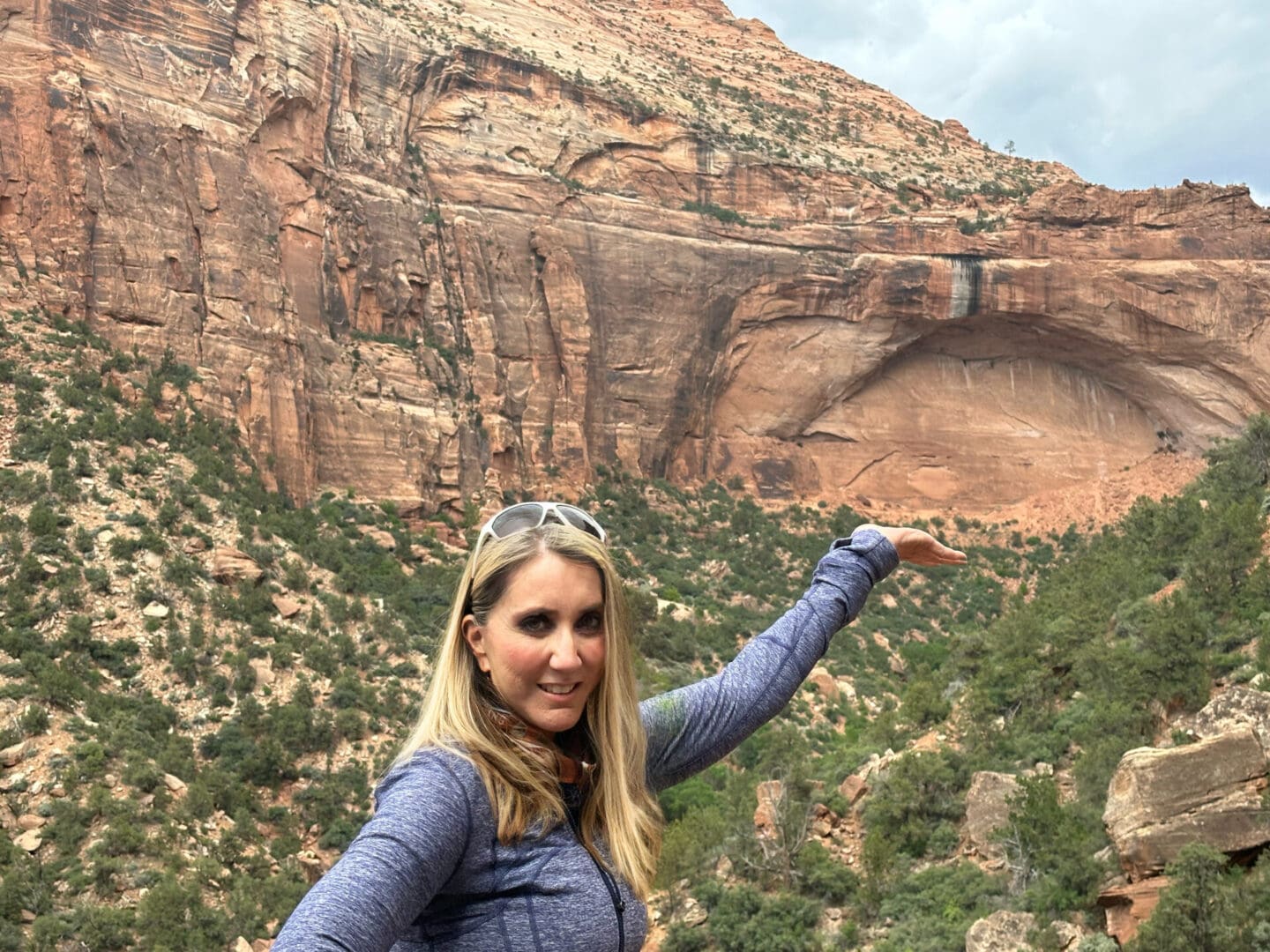 A woman standing in front of a mountain with her hand out.