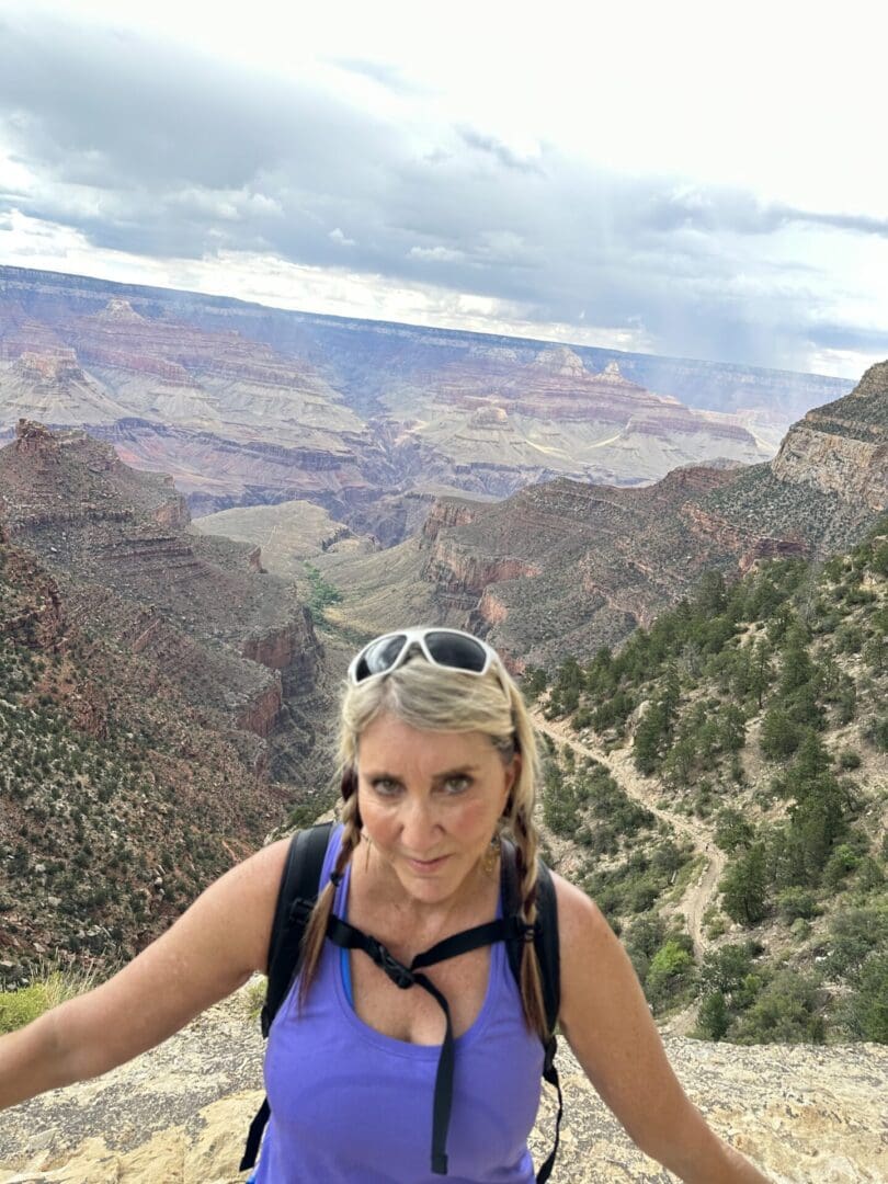 A woman standing on top of a mountain with trees in the background.