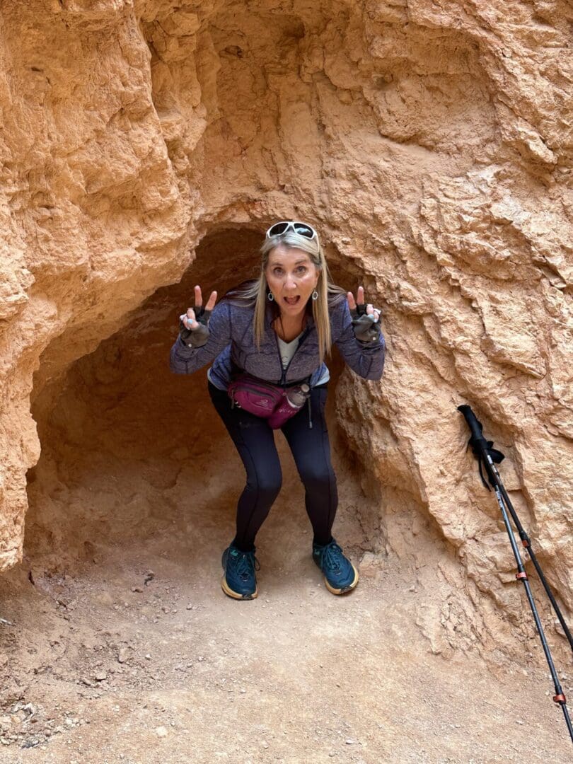 A woman standing in front of a cave with her hands up.