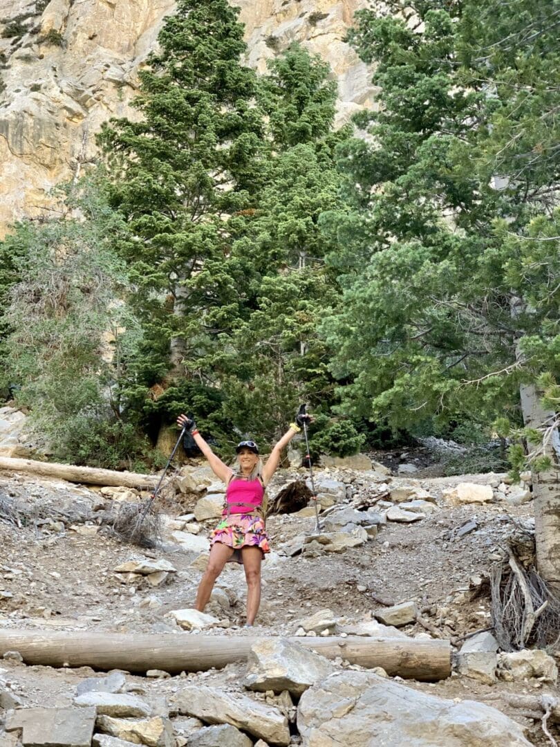 A woman in pink shirt and shorts standing on rocks near trees.