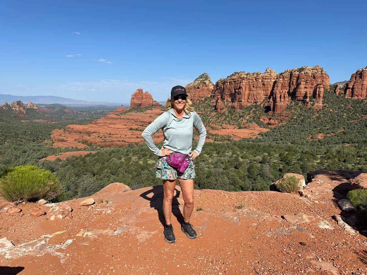 A woman standing on top of a mountain with trees in the background.