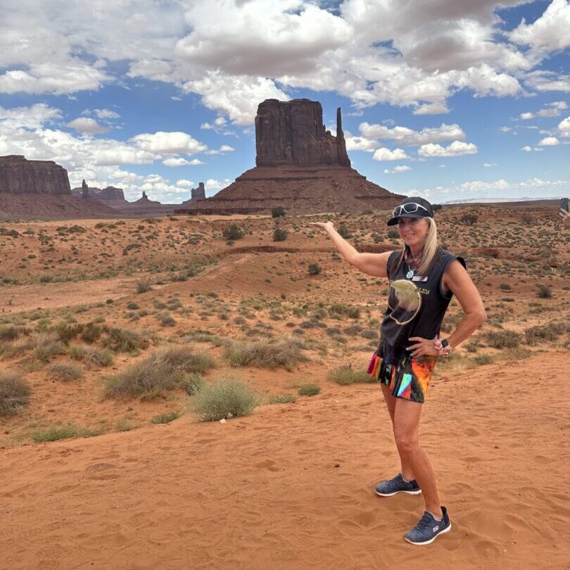 A man in shorts and a hat standing on the desert.